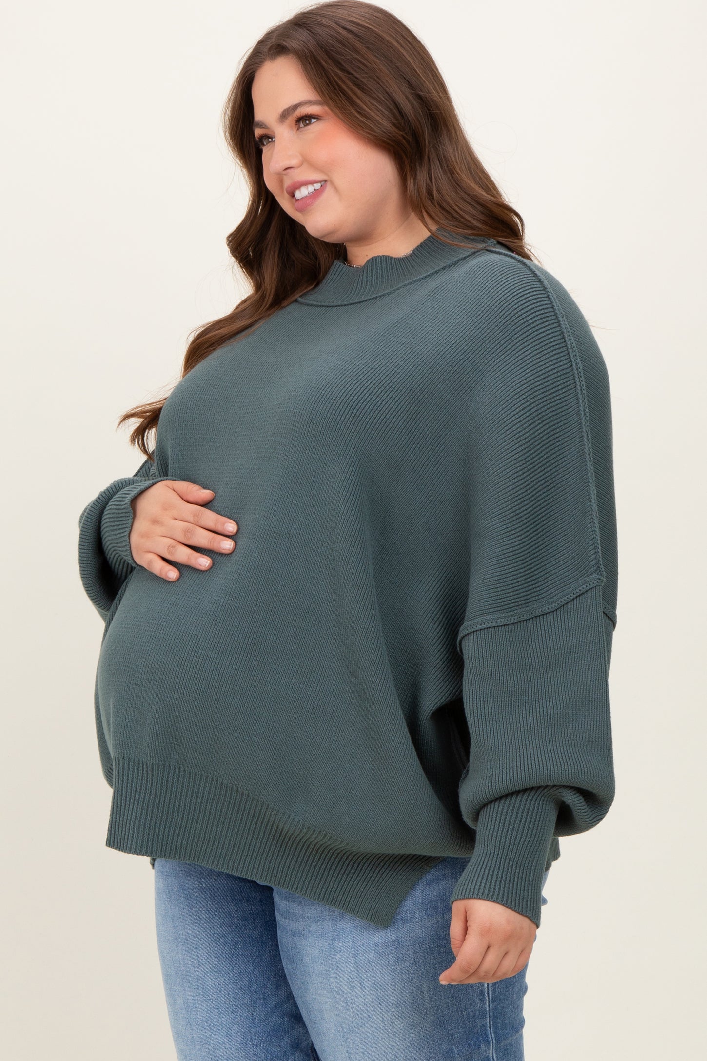 woman wearing a dark green oversized maternity sweater and cradling her baby bump
