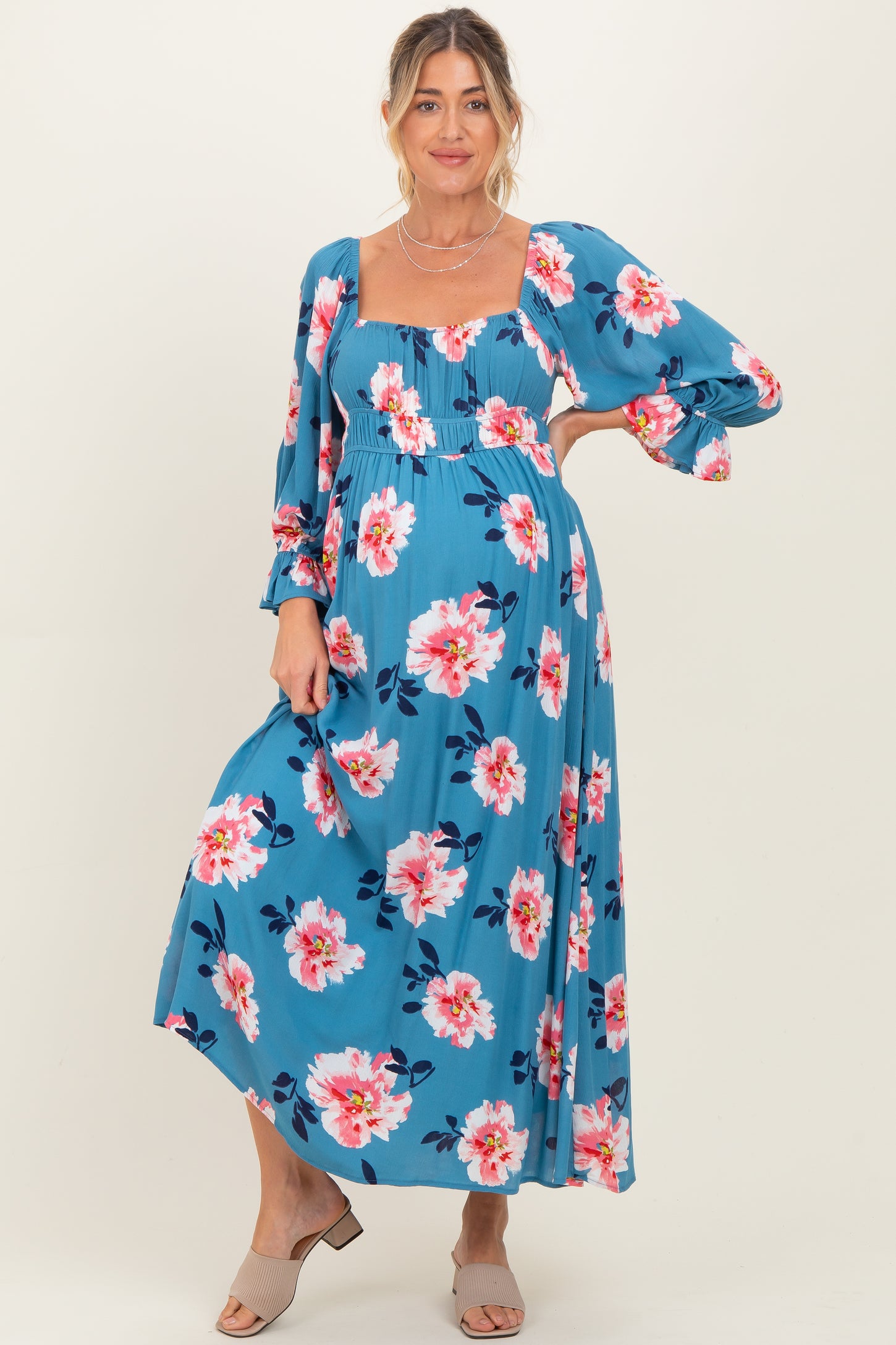 woman wearing a blue floral maternity maxi dress with long sleeves and a square neckline, showcasing her baby bump