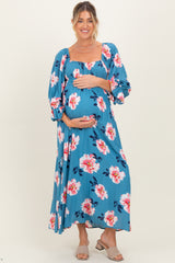 woman wearing a blue floral maternity maxi dress and holding her baby bump
