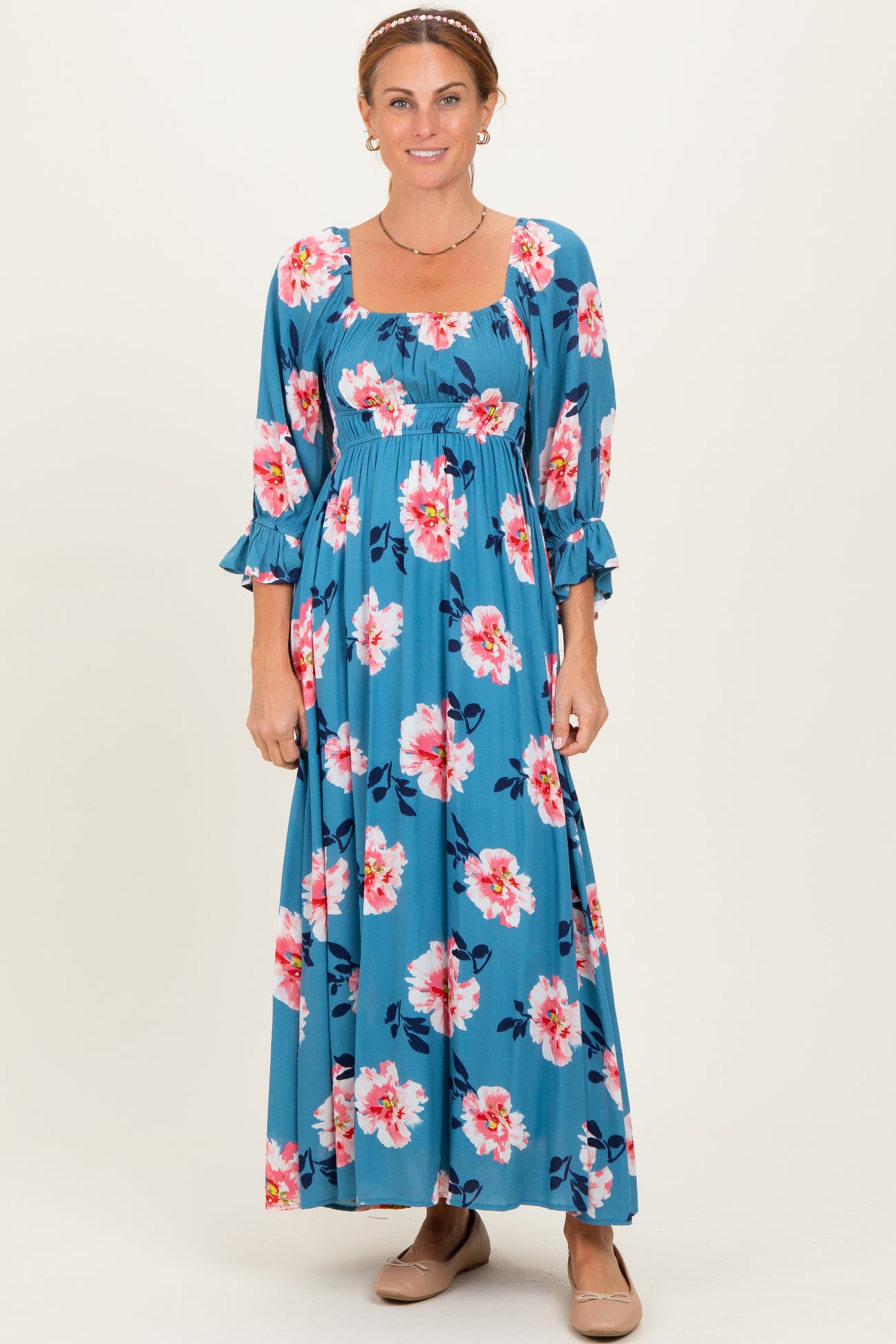 woman wearing a teal floral maxi dress with 3/4 sleeves and ruffle details, smiling at the camera