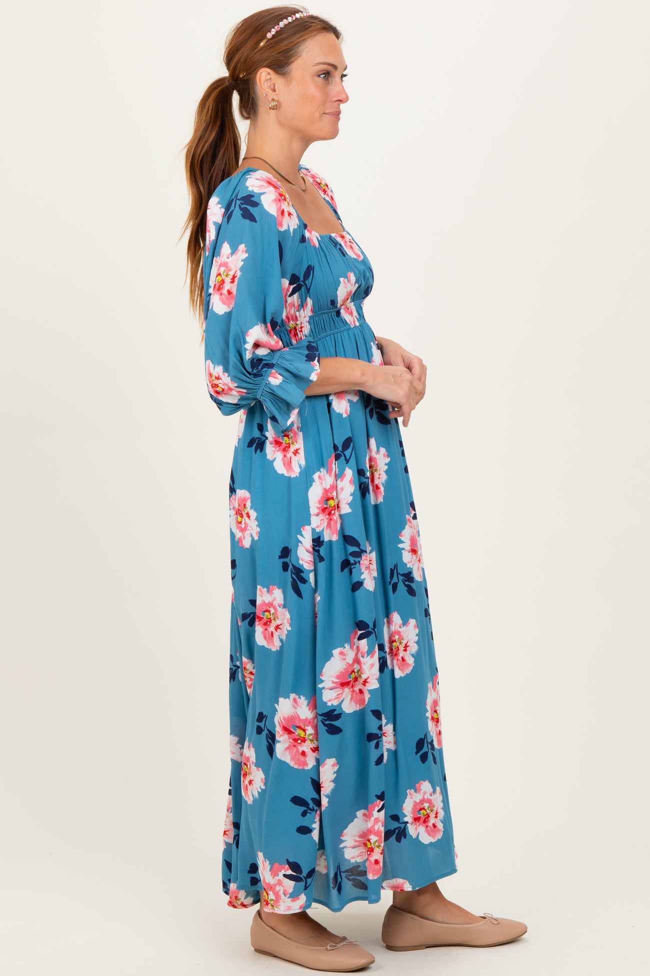 woman wearing a blue floral maxi dress with long sleeves and a fitted bodice, standing sideways