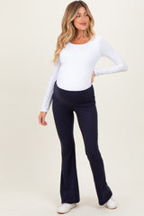 woman wearing a white long sleeve maternity top and navy blue flared maternity pants, showing her baby bump
