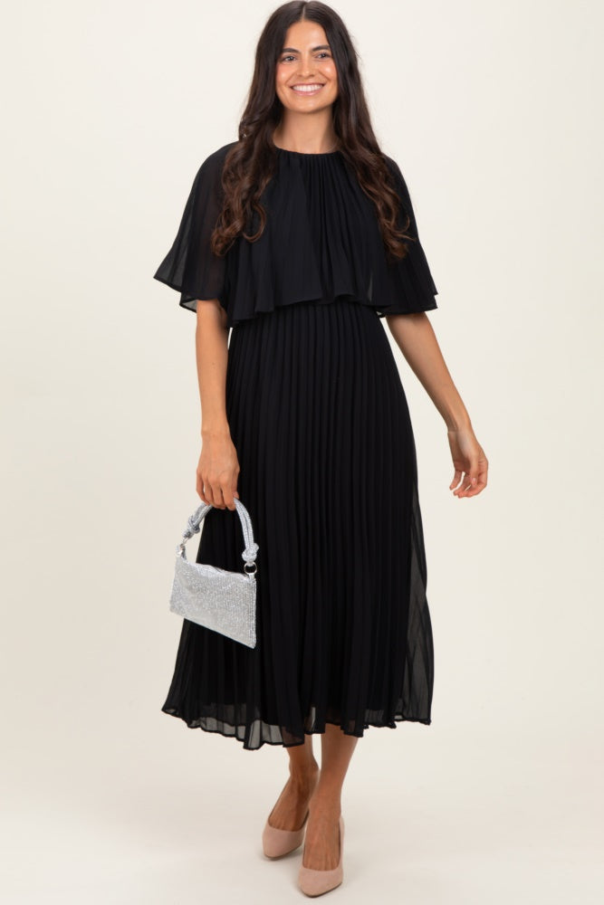woman wearing a black pleated midi dress with a cape overlay and holding a silver embellished handbag