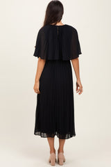 woman wearing a black pleated midi dress with a cape-style back and a flowing silhouette