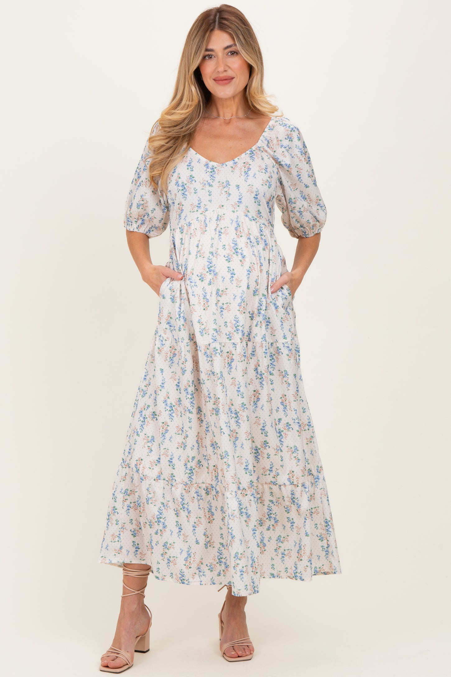 woman wearing a floral print maternity maxi dress with puff sleeves and pockets, showing off her baby bump