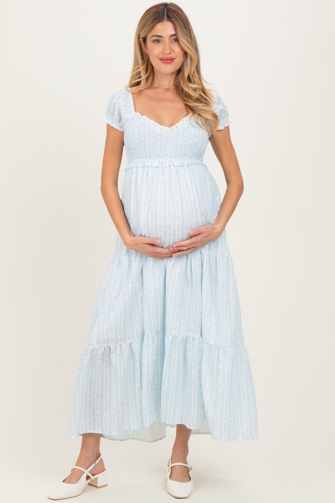 woman wearing a light blue maternity dress with short puff sleeves and a tiered skirt, holding her baby bump