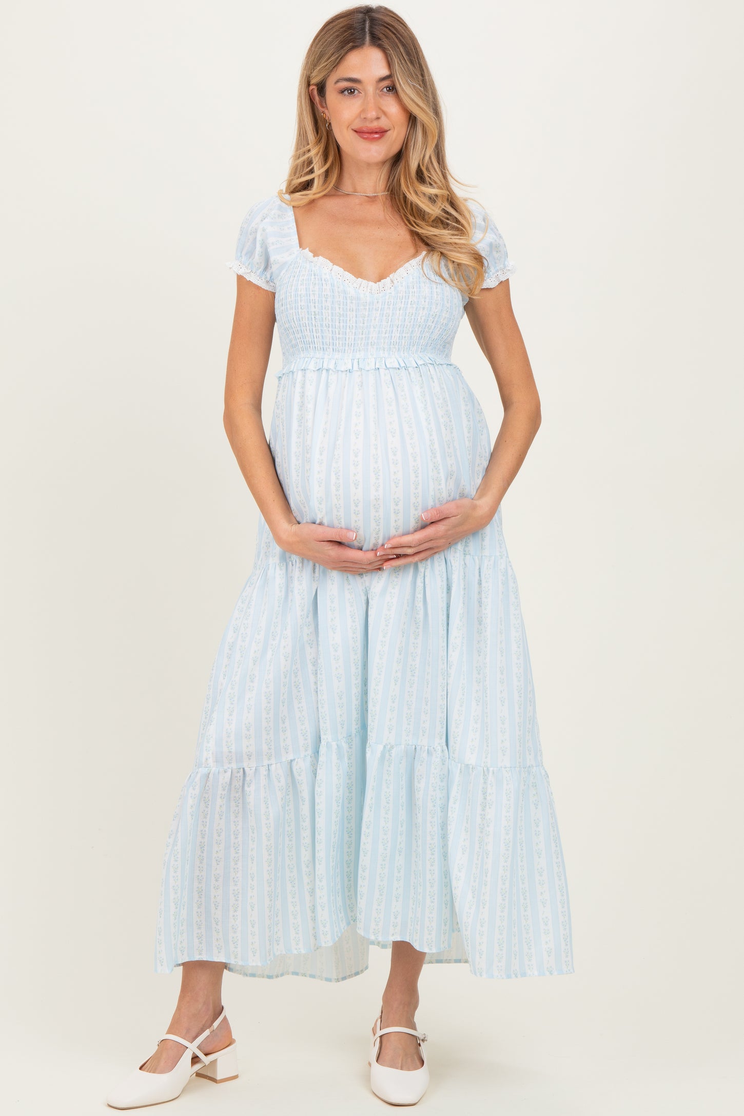 woman wearing a light blue maternity dress with short puff sleeves and a tiered skirt, holding her baby bump