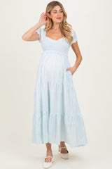 woman wearing a light blue maternity maxi dress with subtle patterns and puff sleeves, showcasing her baby bump
