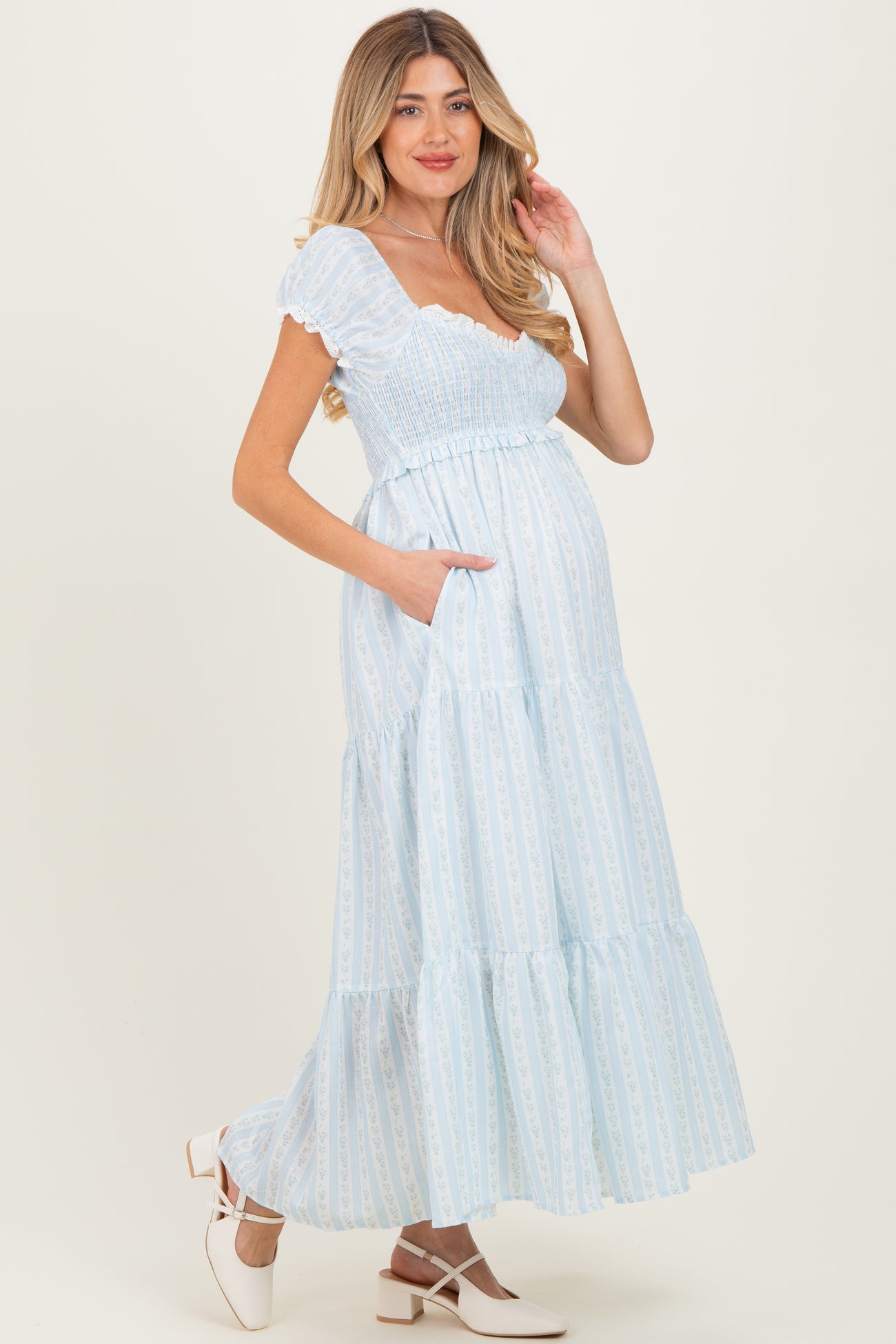 woman wearing a light blue maternity maxi dress with tiered ruffles and pockets, showing a baby bump