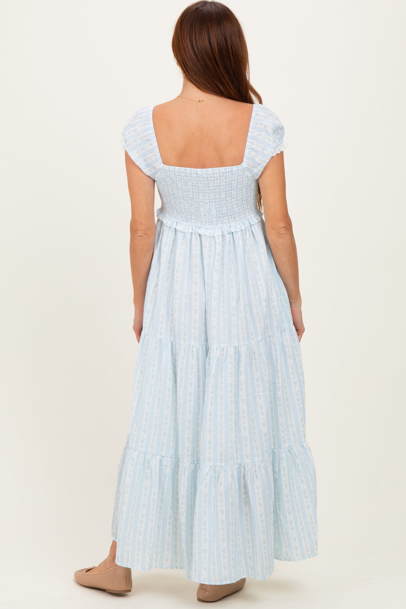 woman wearing a light blue tiered maxi dress with short sleeves and a smocked bodice, shown from the back