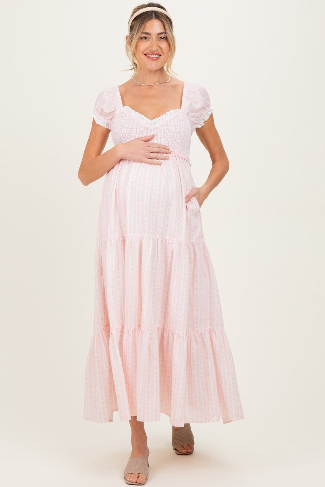 woman wearing a pink maternity maxi dress with puff sleeves and tiered skirt, holding her baby bump
