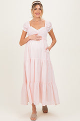 woman wearing a pink maternity maxi dress with puff sleeves and tiered skirt, holding her baby bump