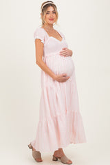 woman wearing a pink maternity maxi dress with puff sleeves and holding her baby bump