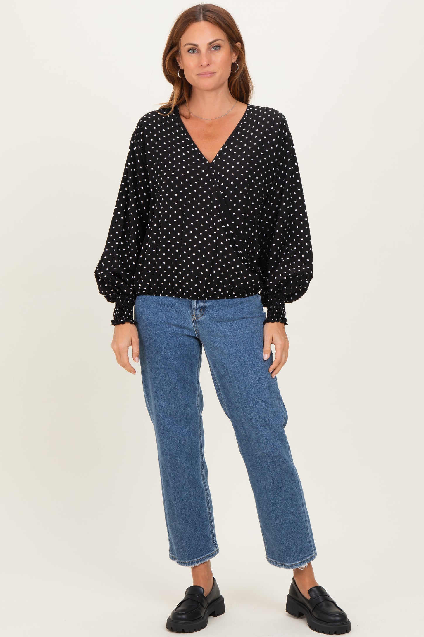 woman wearing a black polka dot wrap top with puffed sleeves and blue high-waisted jeans