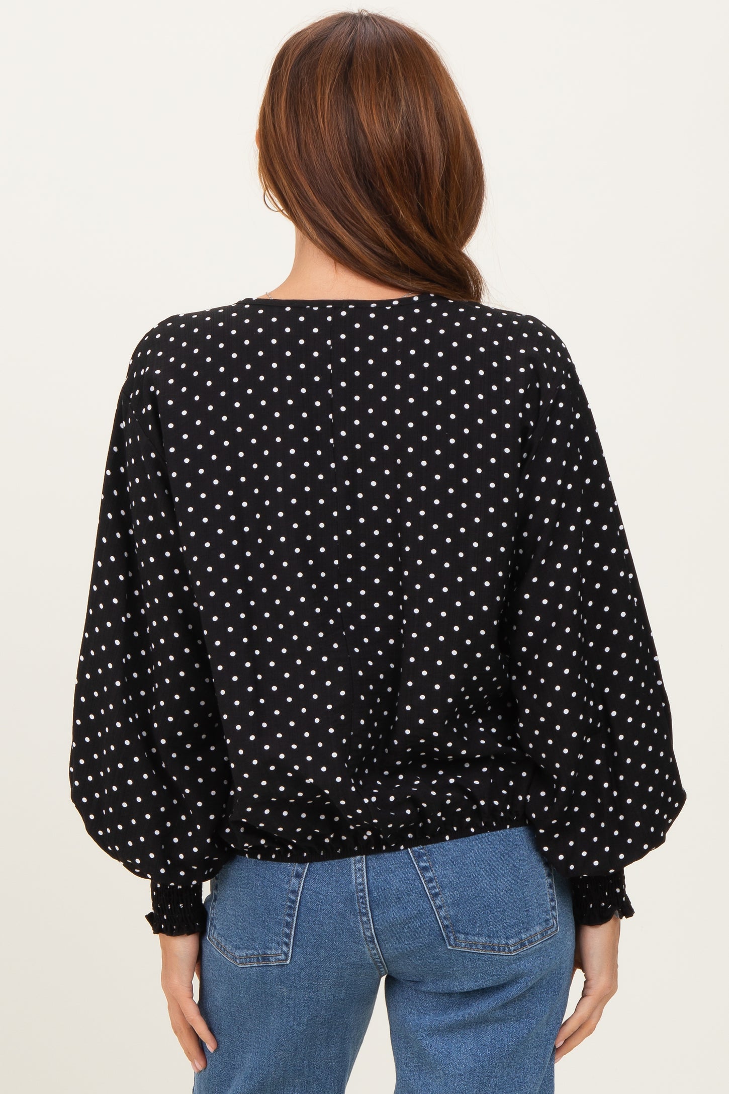 woman wearing a black polka dot blouse with puffed sleeves and a cinched waist, seen from the back