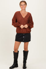 woman wearing a brown polka dot v-neck blouse with puff sleeves and a black denim button-front skirt, paired with knee-high boots