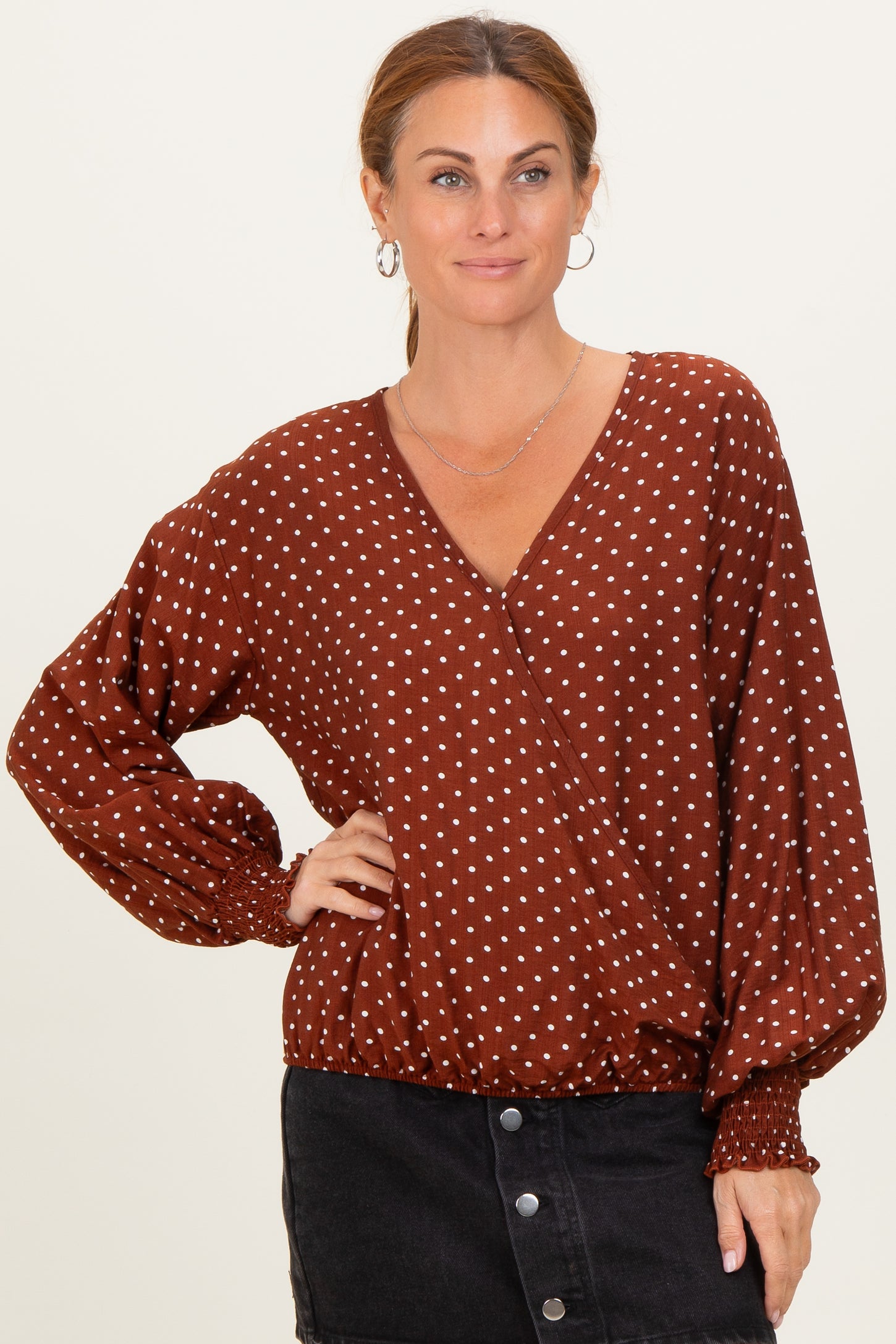 woman wearing a rust brown polka dot wrap top with balloon sleeves and a v-neckline, paired with a black skirt