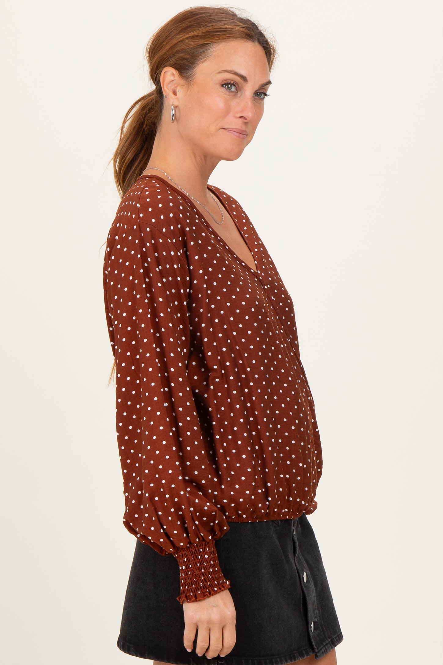 woman wearing a rust colored polka dot blouse with a v-neck and puff sleeves, paired with a black skirt