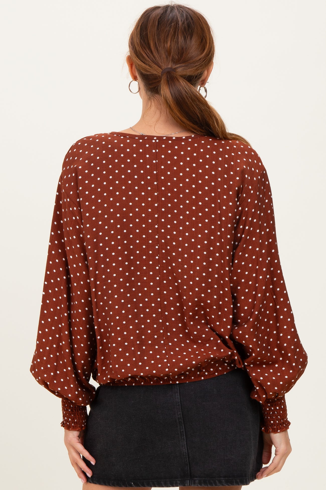 woman wearing a brown polka dot blouse with a relaxed fit and balloon sleeves, viewed from the back