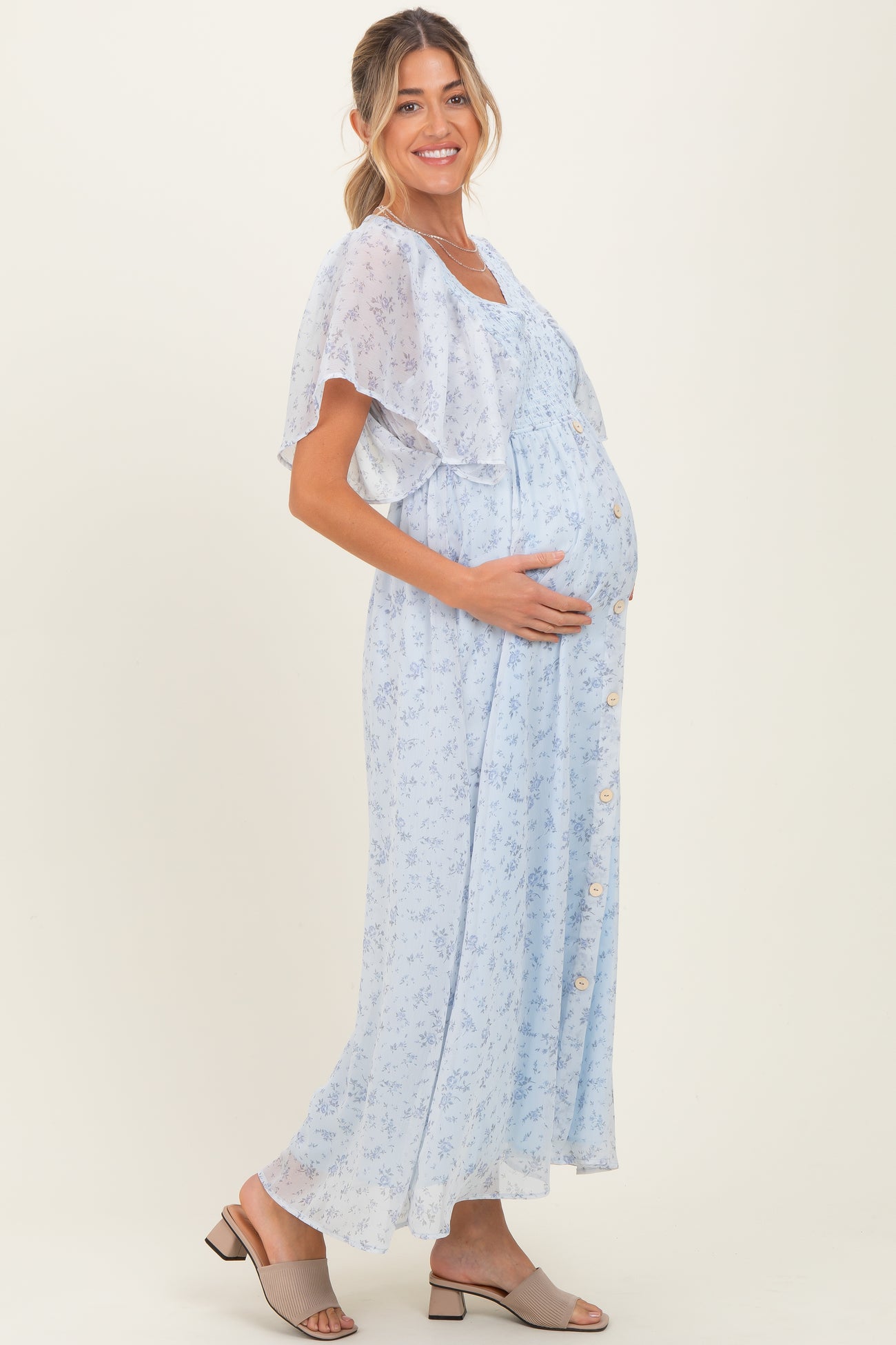 woman wearing a light blue floral maternity dress with a flowing cape sleeve and a visible baby bump