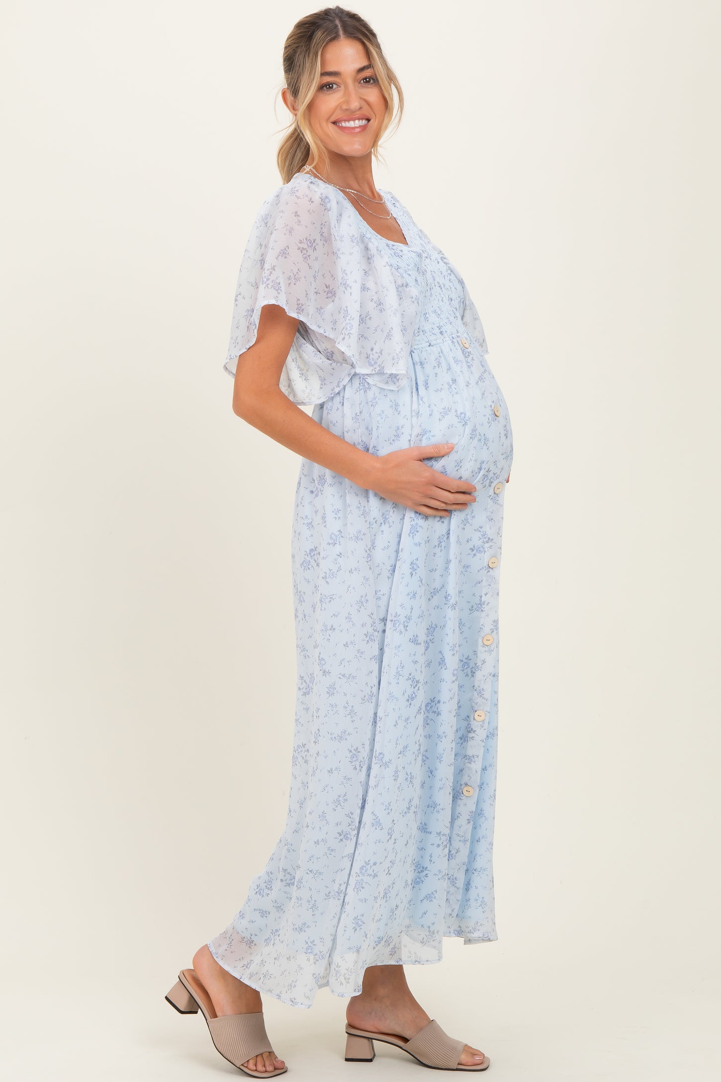 woman wearing a light blue floral maternity dress with a flowing cape sleeve and a visible baby bump
