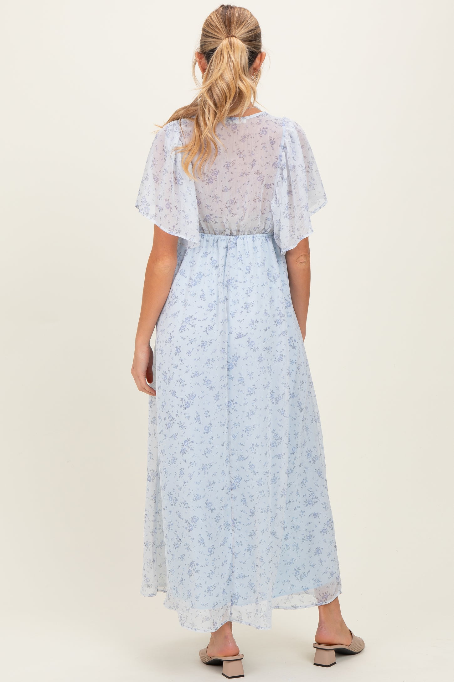 woman wearing a light blue floral maternity maxi dress with flutter sleeves and a cinched waist, showing a baby bump
