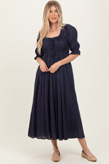 woman wearing a navy blue maxi dress with smocked bodice and puff sleeves, standing with hands on hips