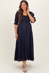 woman wearing a navy blue maternity maxi dress with puff sleeves and a smocked bodice, showing her baby bump