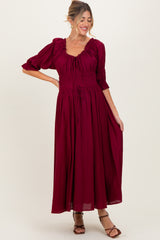 woman wearing a burgundy maternity maxi dress with a smocked bodice and puff sleeves, styled with strappy heels