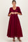 woman wearing a burgundy maternity maxi dress with puff sleeves and a drawstring waist, holding the fabric at the front