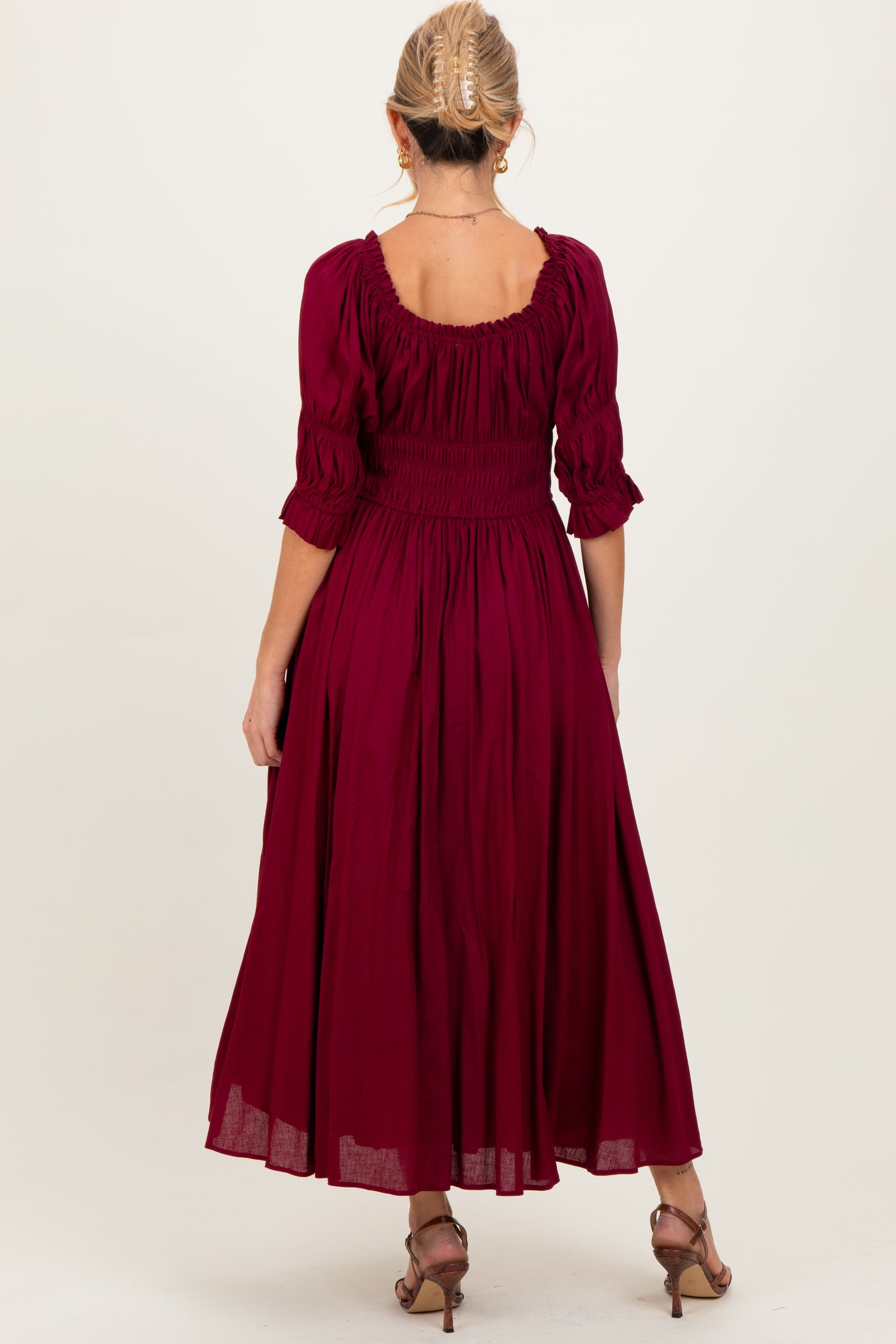 woman wearing a burgundy smocked maternity dress with three-quarter sleeves and a flowy silhouette, seen from the back
