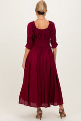 woman wearing a burgundy smocked maternity dress with three-quarter sleeves and a flowy silhouette, seen from the back