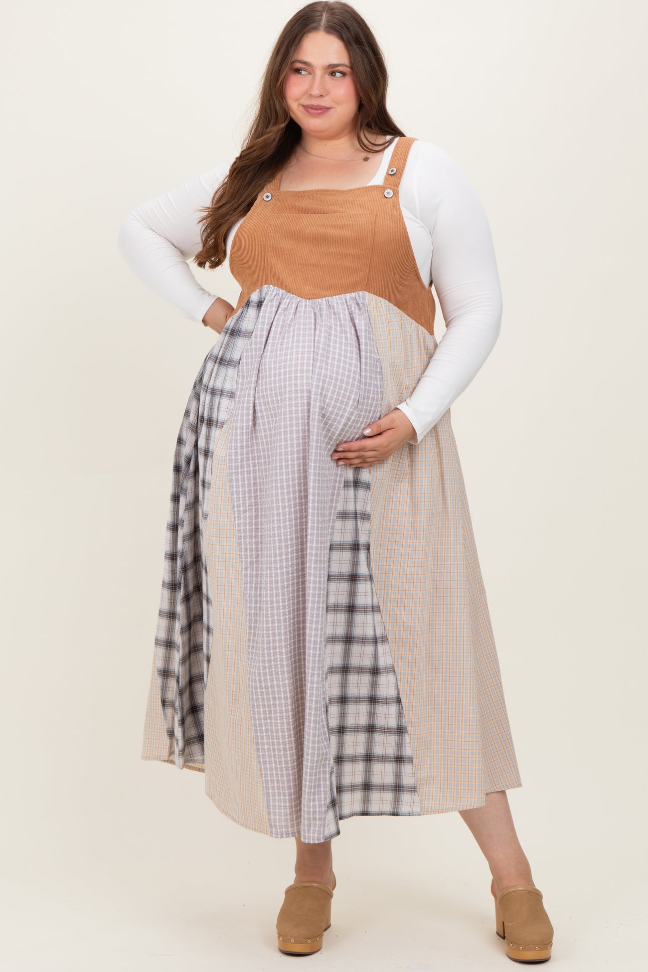 woman wearing a color-blocked maternity plus dress with a brown top and patterned skirt, holding her baby bump