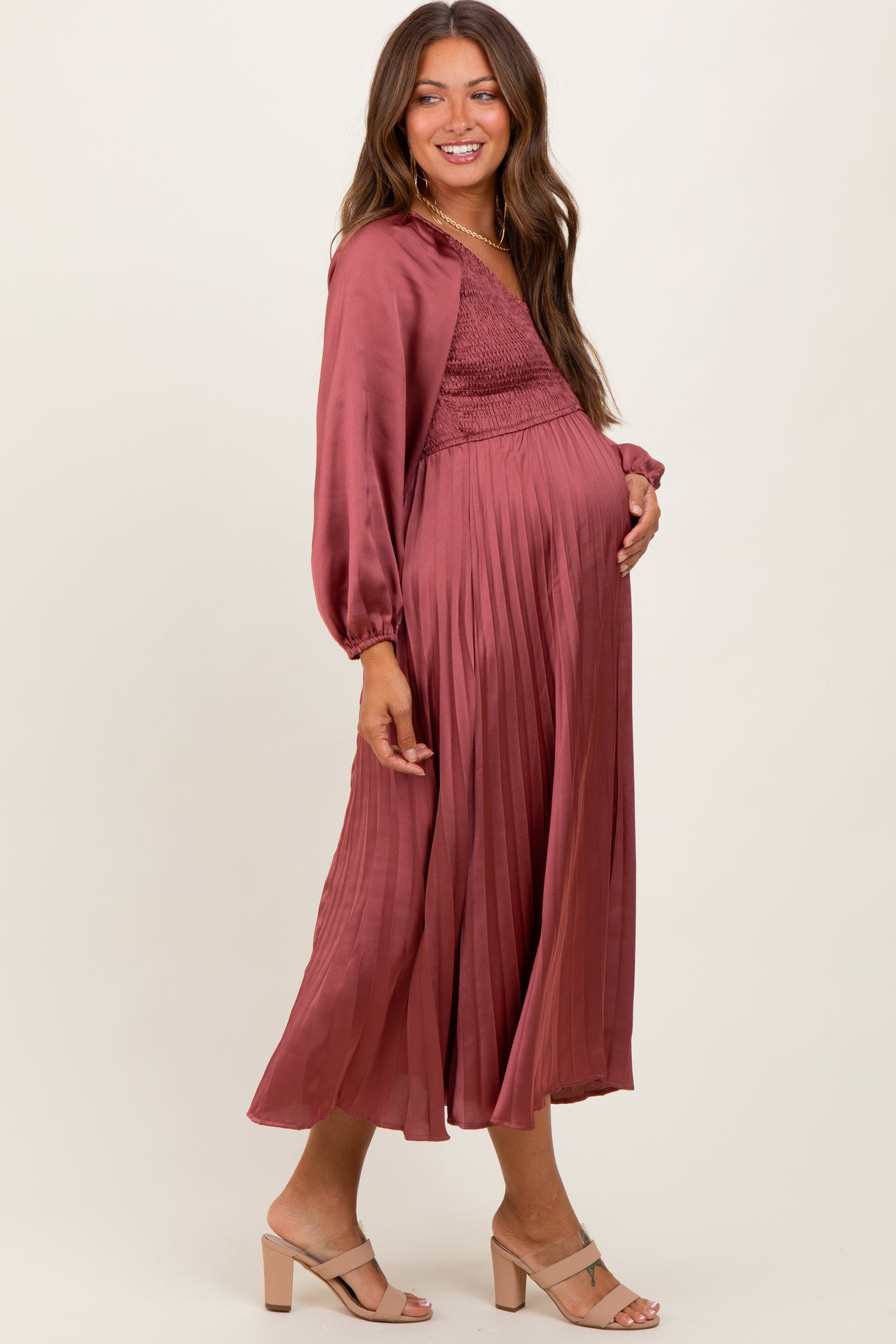 woman wearing a burgundy maternity maxi dress with a smocked bodice and pleated skirt, showing her baby bump