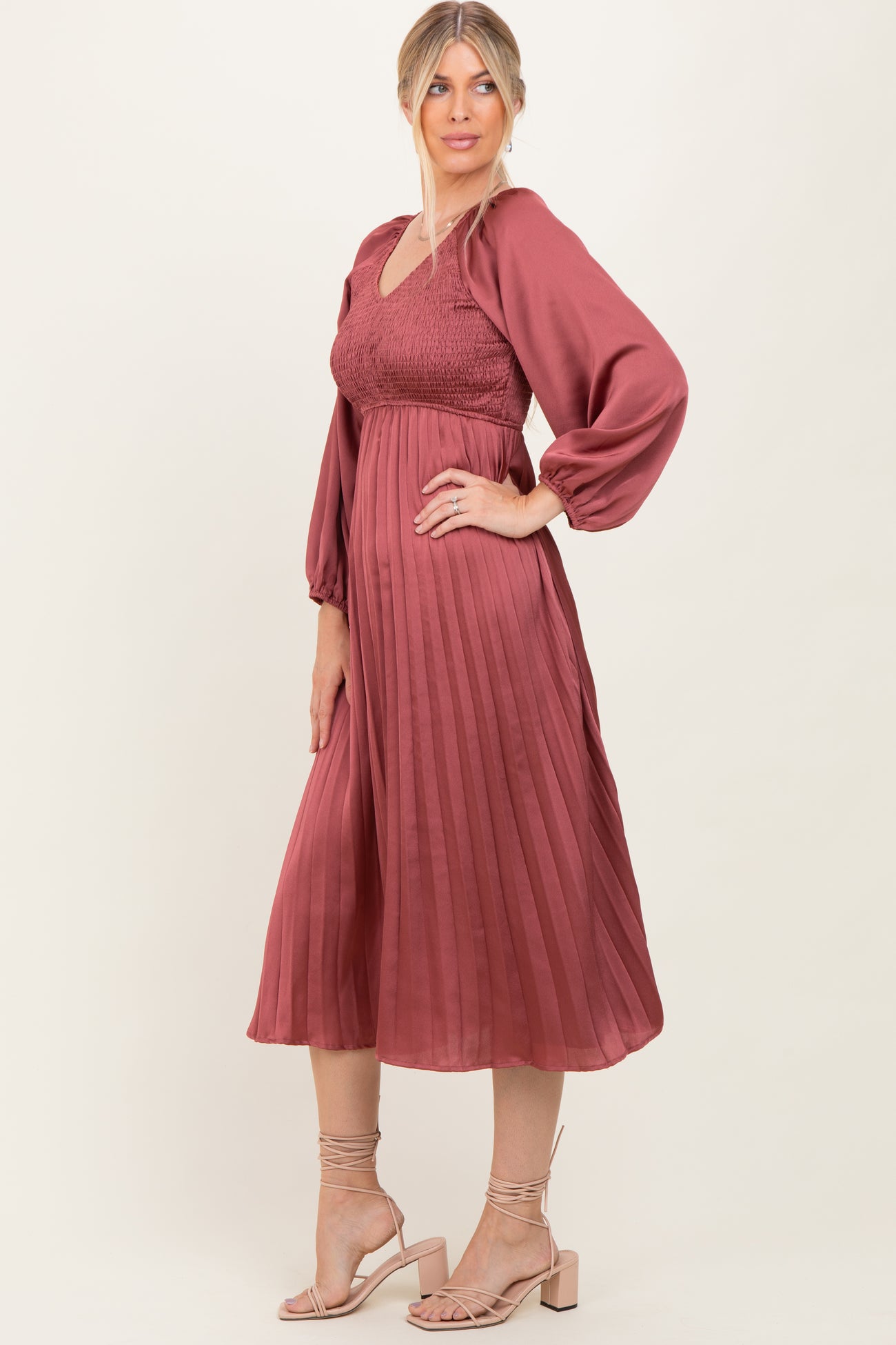 woman wearing a dusty rose pleated midi dress with long puff sleeves and a smocked bodice, styled with strappy heels