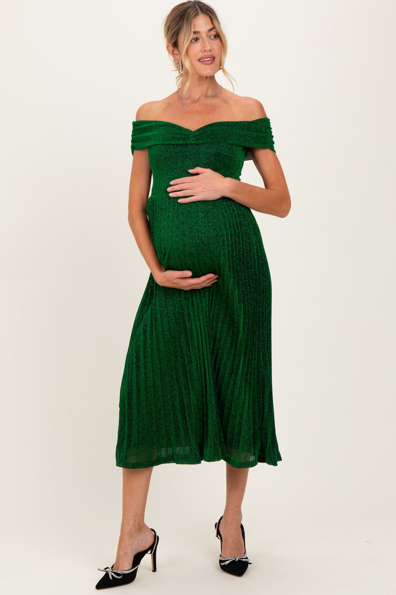 woman wearing a green off-the-shoulder maternity dress with a pleated skirt and holding her baby bump