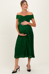 woman wearing a green off-the-shoulder maternity dress with a pleated skirt and holding her baby bump