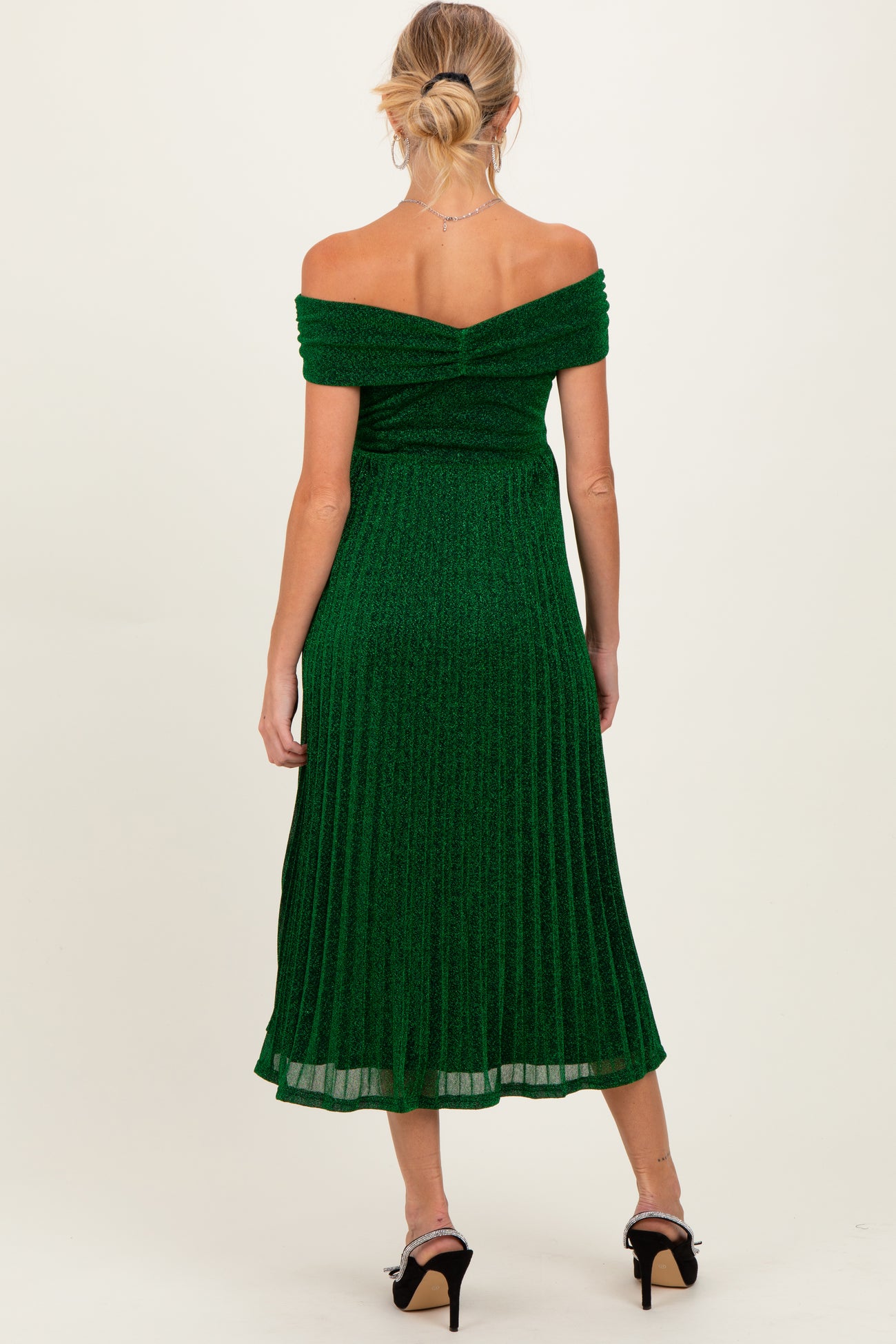 woman wearing an off-shoulder green maternity dress with a pleated design, showing a baby bump from the back
