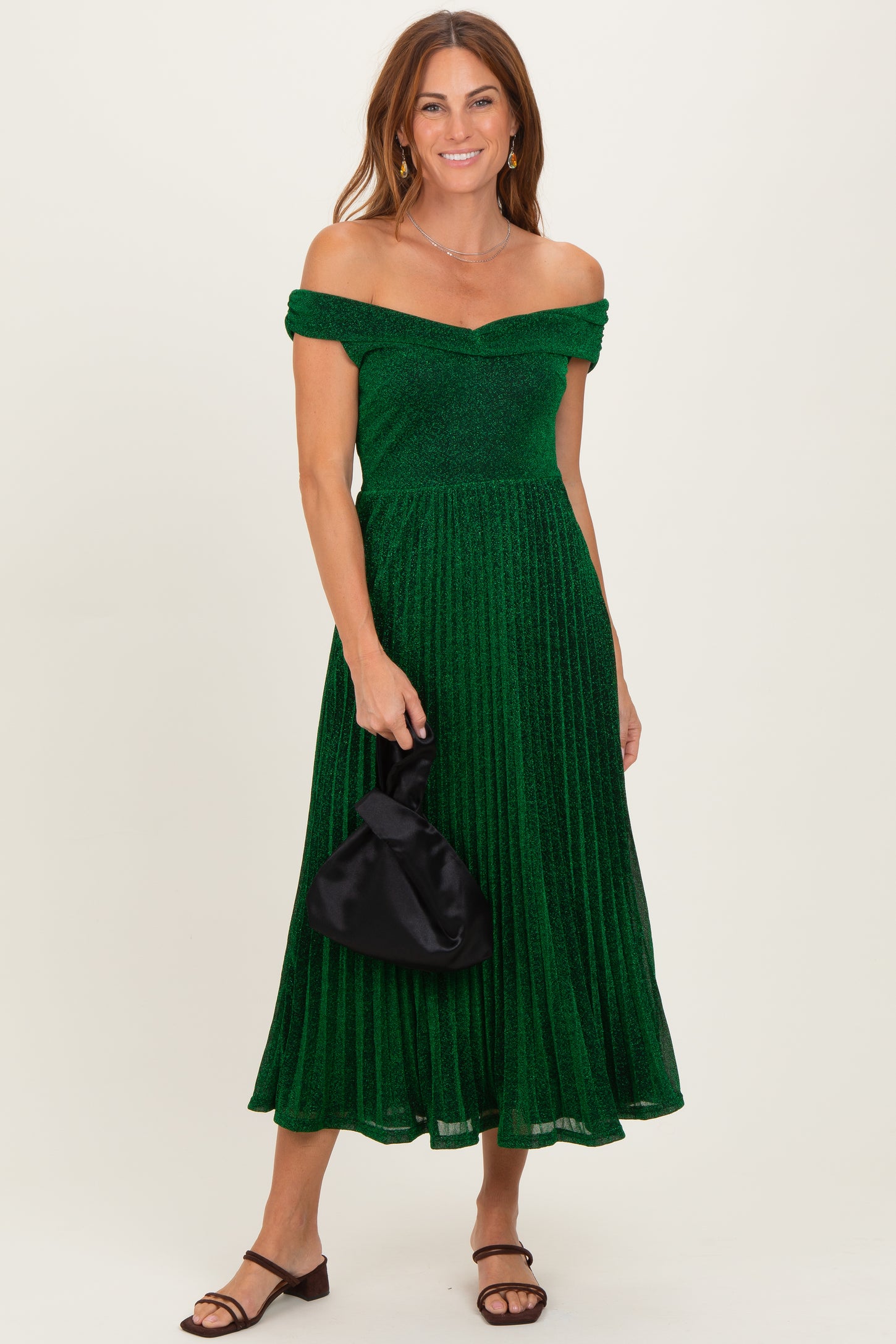 woman wearing a green off-the-shoulder pleated dress and holding a black purse