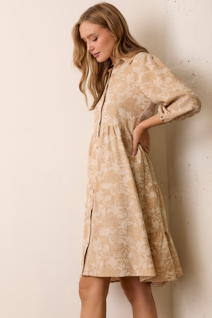woman wearing a beige floral print button-up shirt dress with long sleeves and a tiered skirt