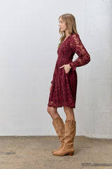 woman wearing a burgundy lace long sleeve dress with a fitted waist and pockets, paired with knee-high tan boots