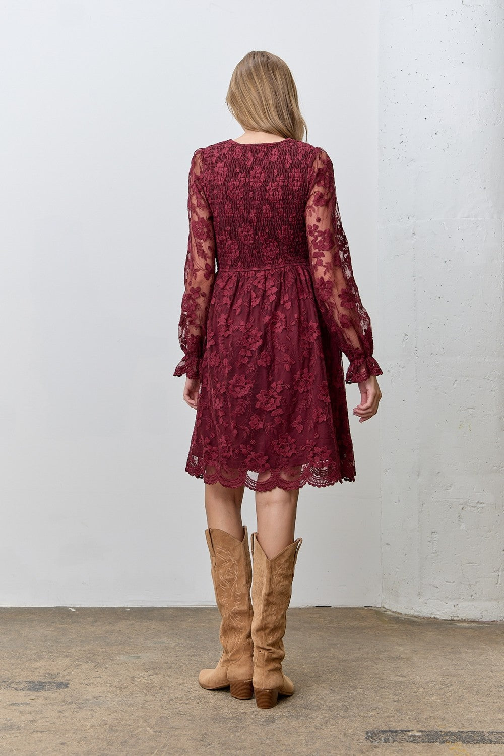 woman wearing a burgundy lace dress with long sleeves and a flared skirt, paired with tan knee-high boots