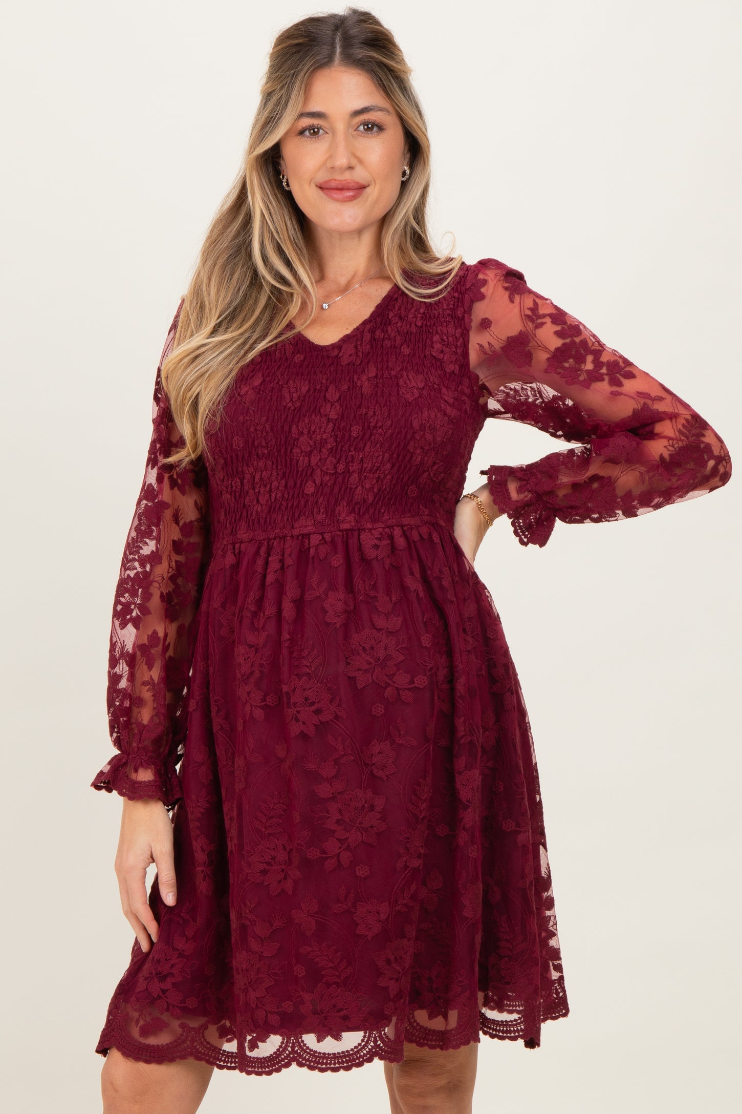 woman wearing a burgundy lace maternity dress with long sheer sleeves and a fit-and-flare silhouette