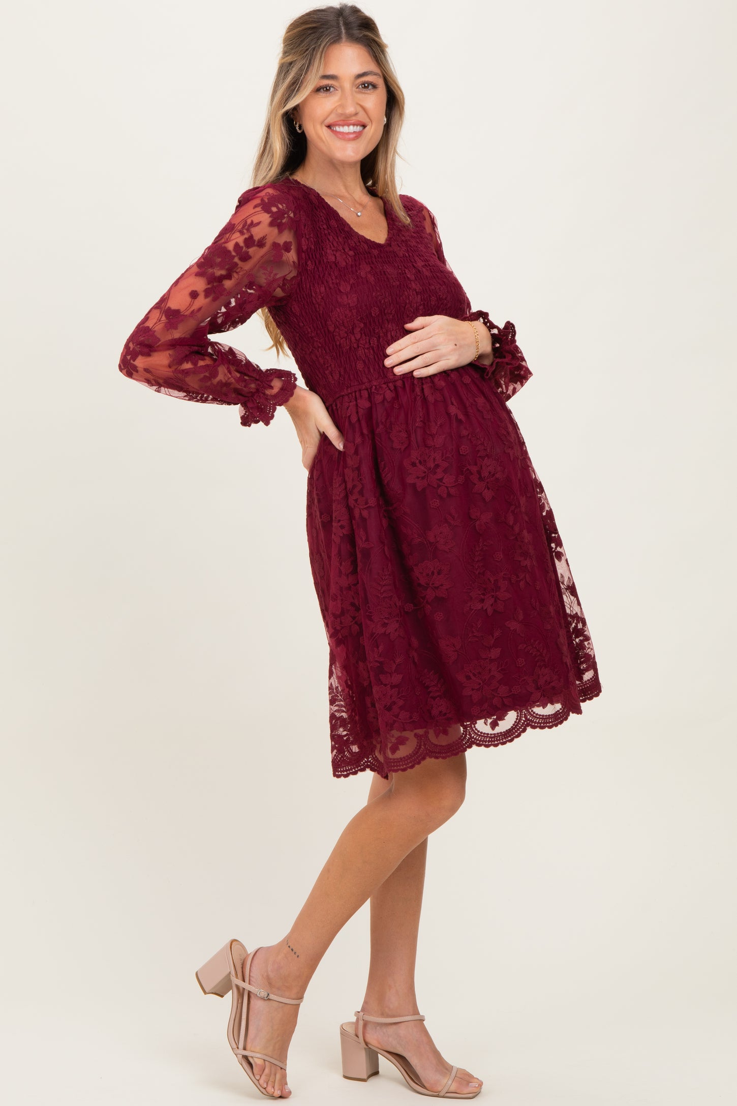 woman wearing a burgundy lace maternity dress with long sleeves and holding her baby bump