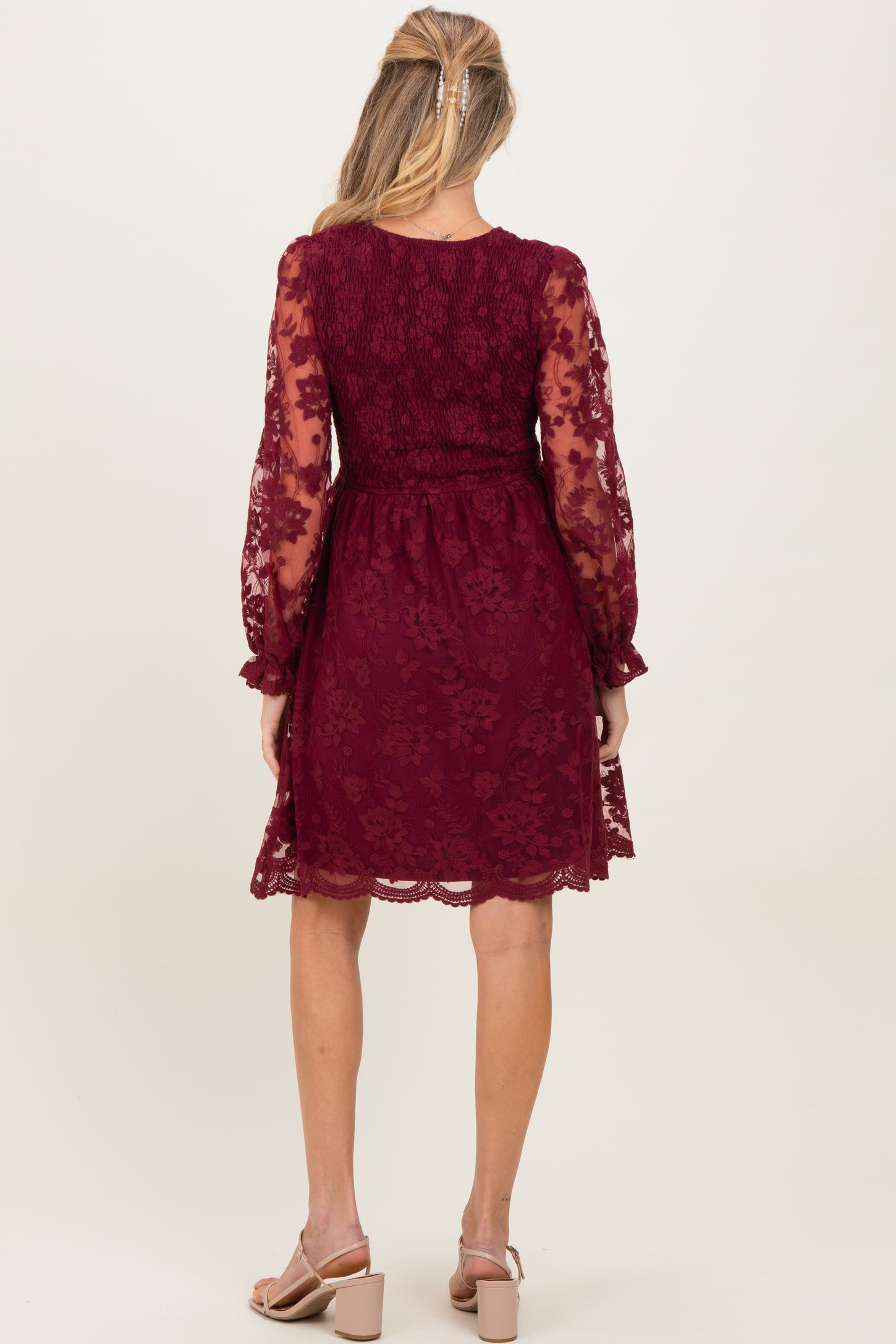 woman wearing a burgundy lace maternity dress with long sheer sleeves and a fitted bodice, showing a baby bump from the back