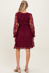 woman wearing a burgundy lace maternity dress with long sheer sleeves and a fitted bodice, showing a baby bump from the back
