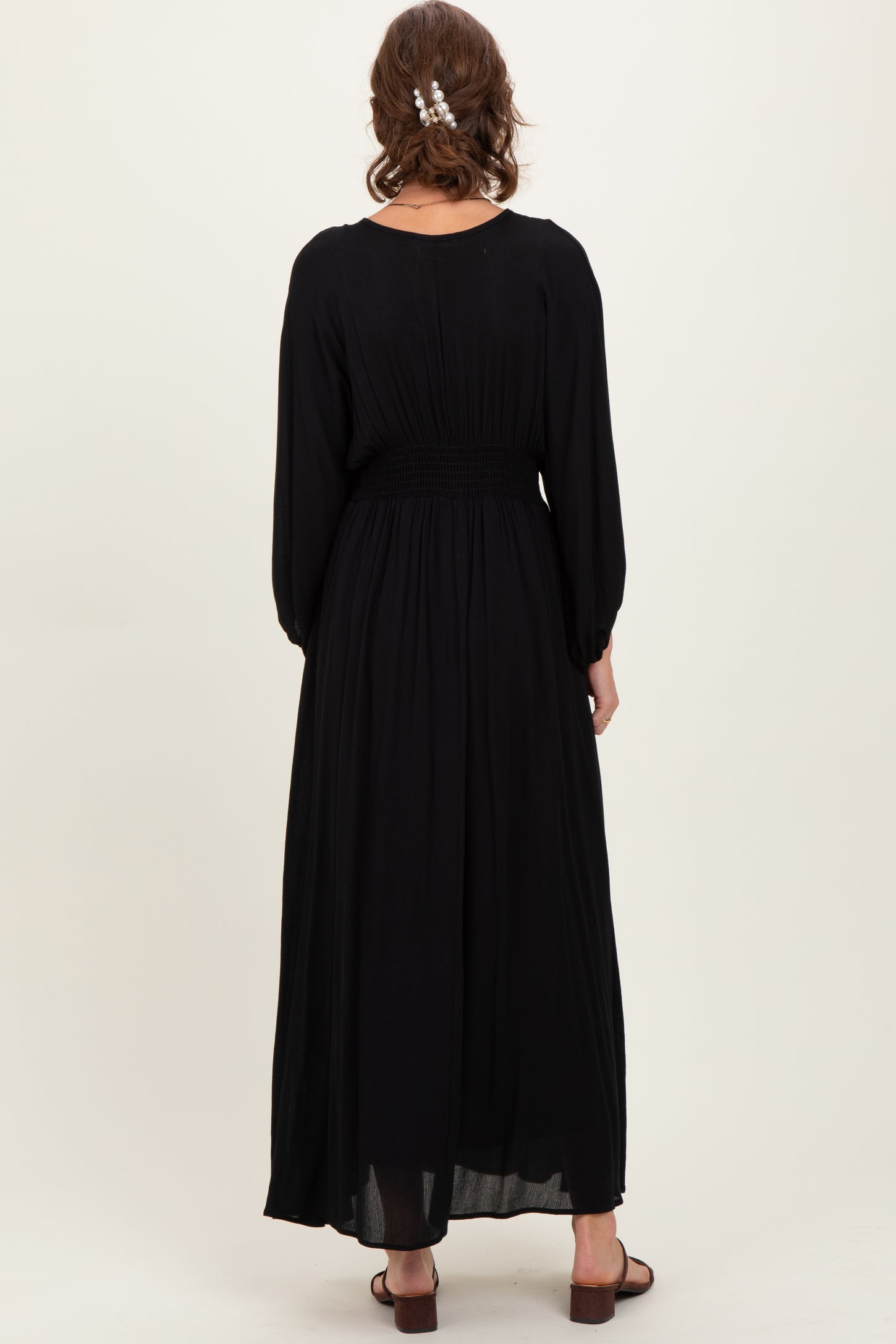 woman wearing a black long sleeve maxi dress with a smocked waistband, shown from the back