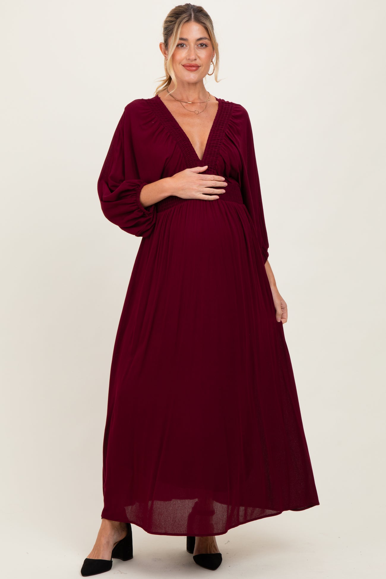 woman wearing a burgundy maternity maxi dress with puff sleeves and a v-neck, holding her baby bump