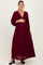 woman wearing a burgundy maternity maxi dress with puff sleeves and a v-neck, holding her baby bump