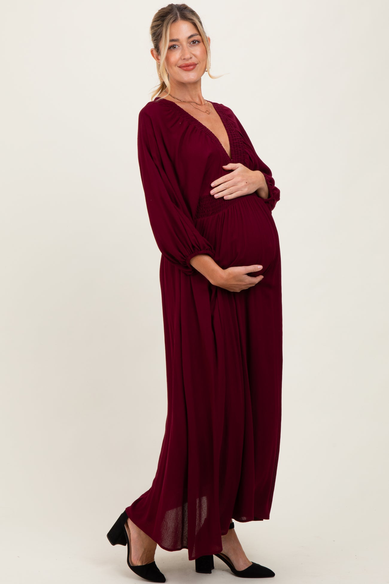woman wearing a burgundy long sleeve maternity dress with a deep v-neck and a visible baby bump